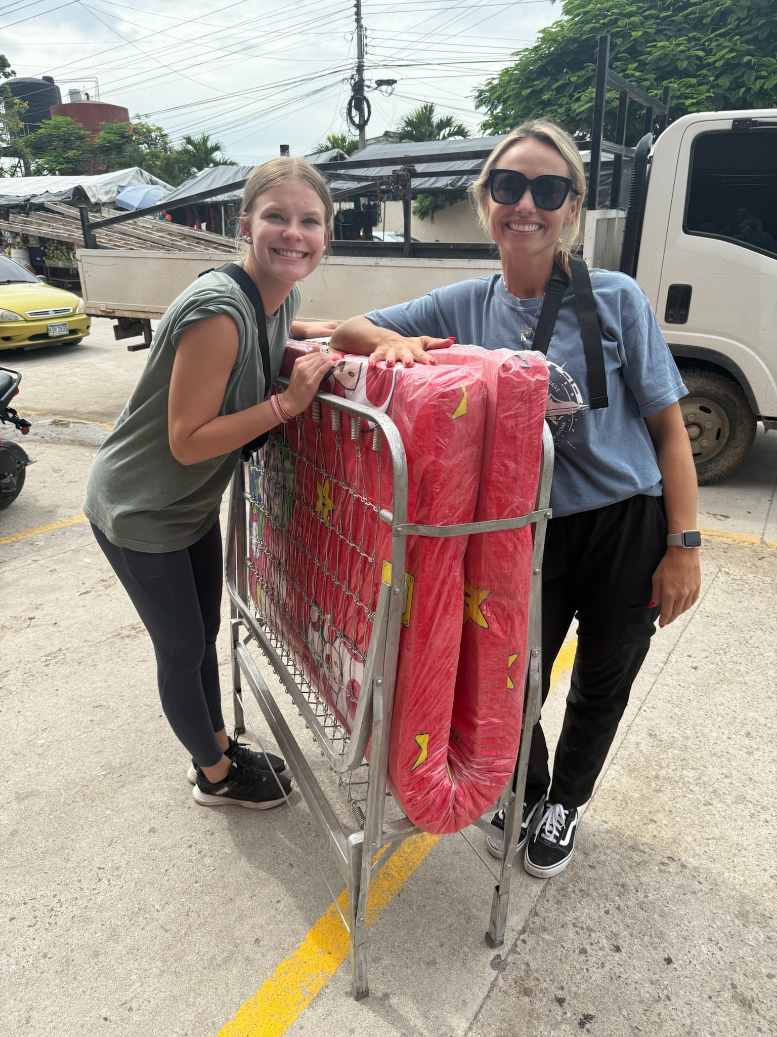 Two women holding a pink fabric roll outdoors