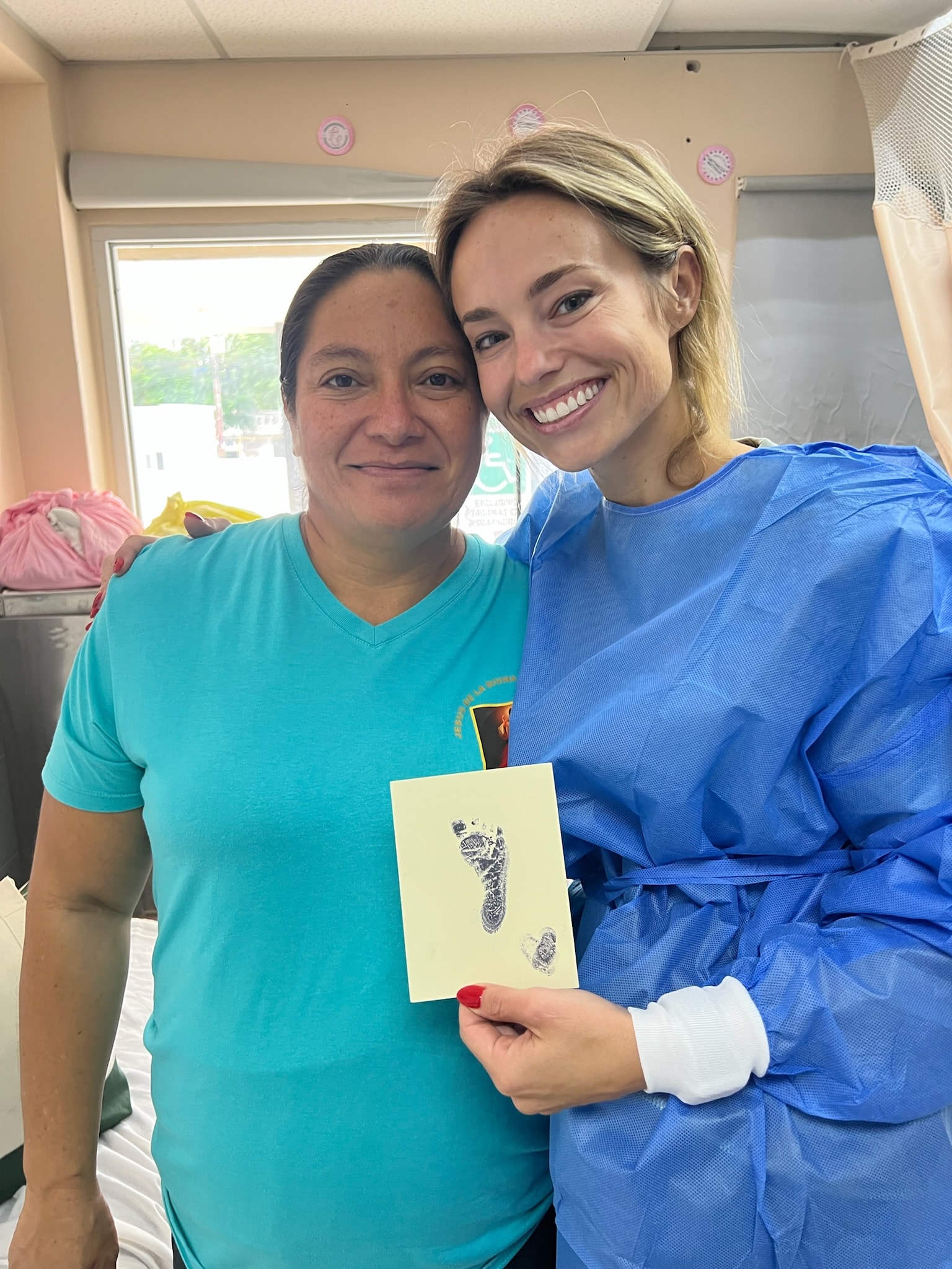 Two women holding a baby footprint card indoors